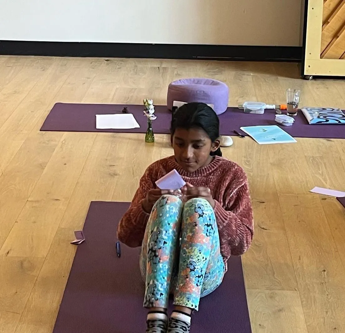A child reading an affirmation card on a yoga mat
